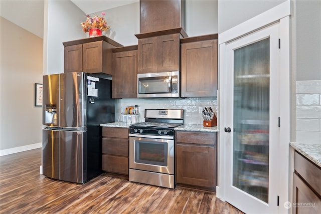 kitchen with light stone countertops, appliances with stainless steel finishes, backsplash, vaulted ceiling, and dark wood-type flooring