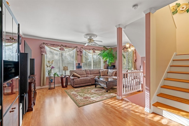 living area featuring baseboards, ceiling fan, stairs, light wood-type flooring, and ornate columns