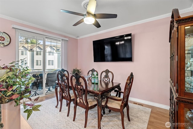 dining room with crown molding, visible vents, a ceiling fan, wood finished floors, and baseboards