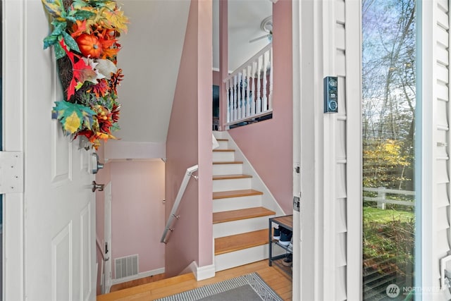 stairway with a wealth of natural light, ceiling fan, visible vents, and wood finished floors