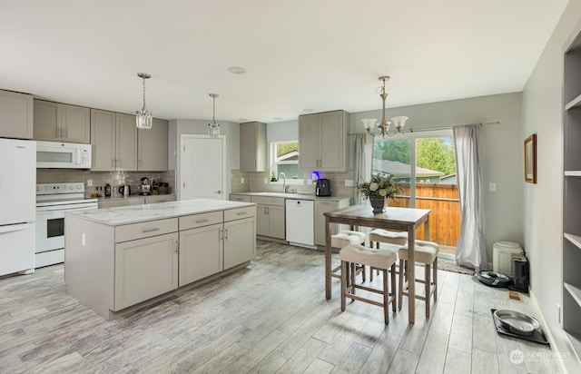 kitchen with light hardwood / wood-style flooring, decorative light fixtures, white appliances, gray cabinets, and a kitchen island