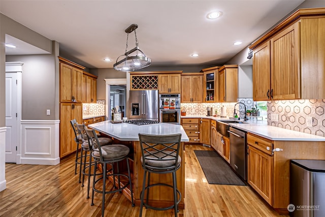 kitchen with decorative light fixtures, a kitchen island, light hardwood / wood-style floors, and appliances with stainless steel finishes