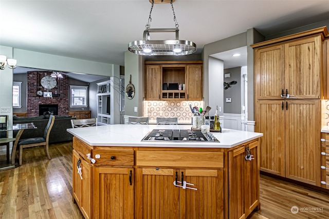 kitchen with an inviting chandelier, a fireplace, a kitchen island, wood-type flooring, and stainless steel gas cooktop