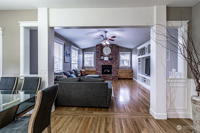 living room with ceiling fan, dark wood-type flooring, lofted ceiling, and a brick fireplace