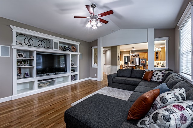 living room featuring built in features, ceiling fan with notable chandelier, wood-type flooring, and vaulted ceiling