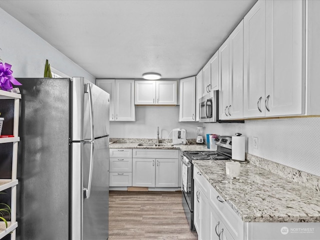 kitchen featuring appliances with stainless steel finishes, light wood-type flooring, white cabinets, light stone counters, and sink