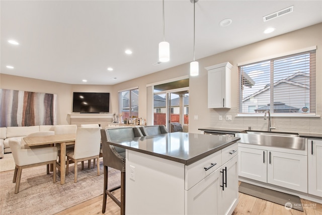 kitchen with tasteful backsplash, light hardwood / wood-style flooring, decorative light fixtures, a kitchen bar, and white cabinets