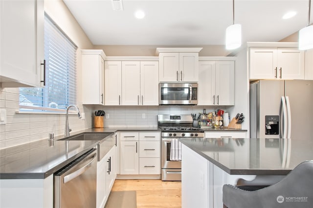 kitchen featuring white cabinets, hanging light fixtures, light hardwood / wood-style flooring, decorative backsplash, and stainless steel appliances