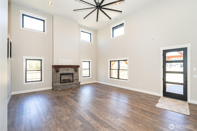 unfurnished living room featuring baseboards, a stone fireplace, a towering ceiling, and dark wood-style flooring