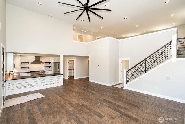 unfurnished living room featuring baseboards, dark wood-style floors, recessed lighting, and stairs