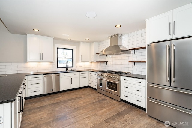 kitchen featuring wall chimney exhaust hood, dark countertops, a sink, and high quality appliances
