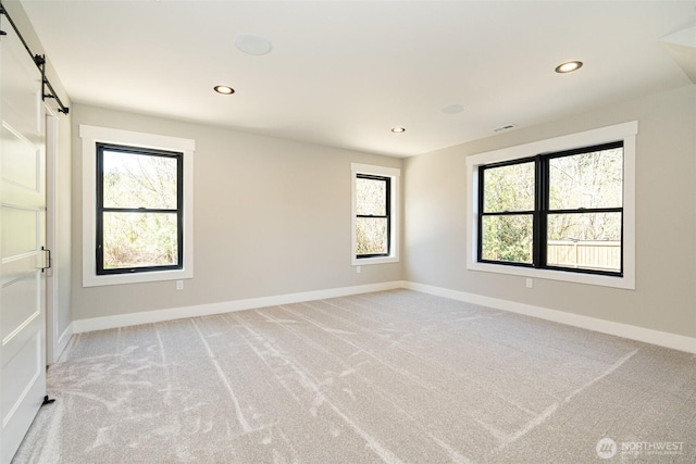 empty room with a barn door, a healthy amount of sunlight, baseboards, and light carpet