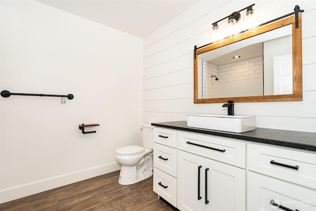 bathroom featuring wood finished floors, toilet, vanity, baseboards, and walk in shower