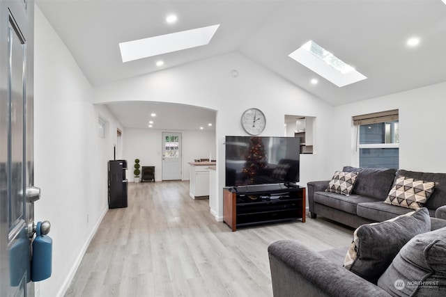 living room with a skylight, high vaulted ceiling, and light hardwood / wood-style floors