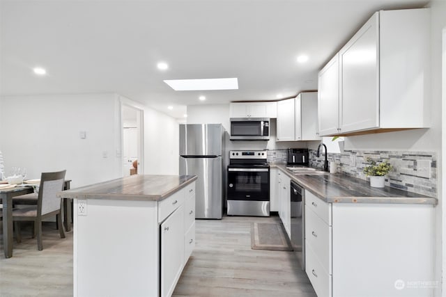 kitchen with a skylight, sink, stainless steel appliances, light hardwood / wood-style flooring, and white cabinets