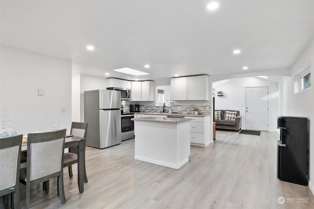 kitchen with a skylight, white cabinetry, a center island, appliances with stainless steel finishes, and light wood-type flooring