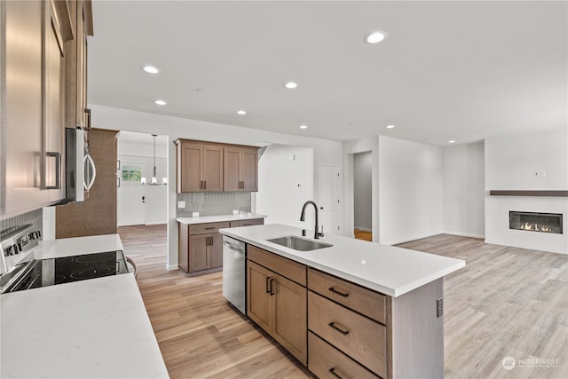 kitchen featuring sink, a center island with sink, light hardwood / wood-style flooring, stainless steel appliances, and decorative backsplash