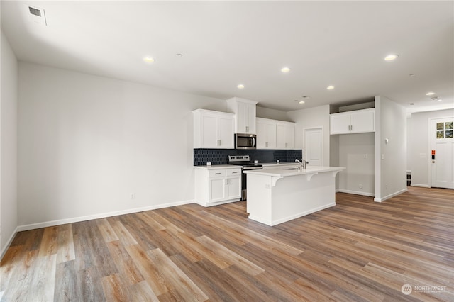 kitchen featuring white cabinetry, sink, stainless steel appliances, light hardwood / wood-style flooring, and an island with sink