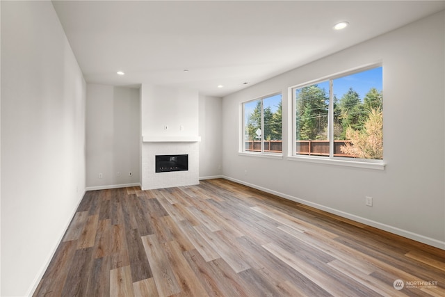 unfurnished living room featuring a glass covered fireplace, recessed lighting, baseboards, and wood finished floors