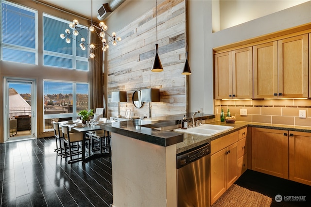 kitchen featuring pendant lighting, dishwasher, wood walls, sink, and a towering ceiling