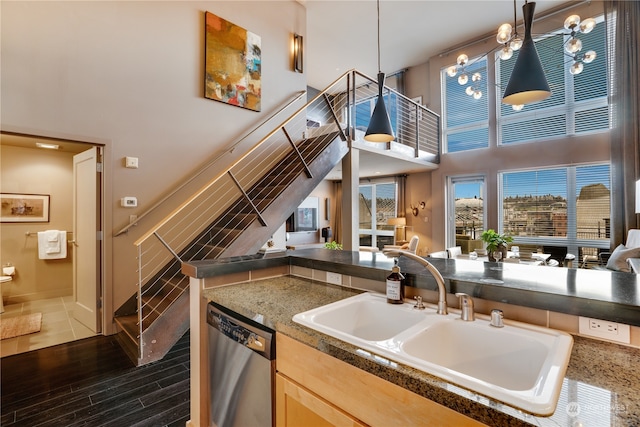 kitchen featuring sink, stainless steel dishwasher, dark hardwood / wood-style floors, a towering ceiling, and decorative light fixtures