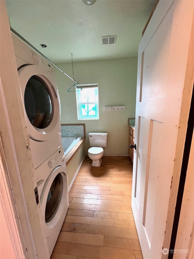 washroom with light hardwood / wood-style flooring and stacked washing maching and dryer