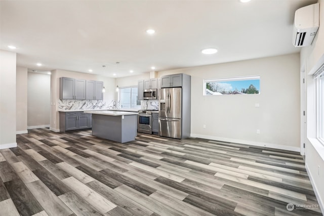 kitchen featuring appliances with stainless steel finishes, a center island, a wall mounted AC, and gray cabinetry