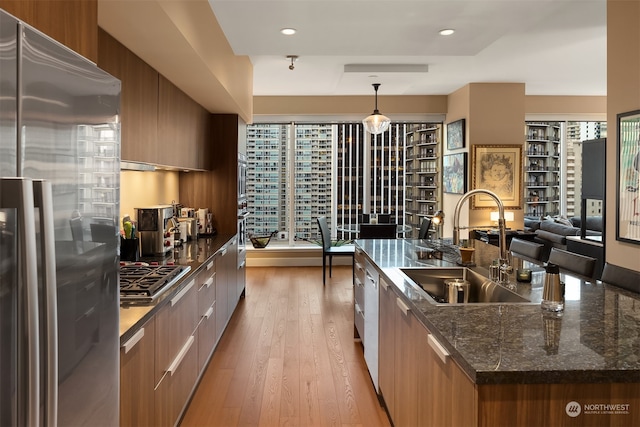 kitchen featuring sink, hanging light fixtures, stainless steel appliances, a large island with sink, and light hardwood / wood-style floors