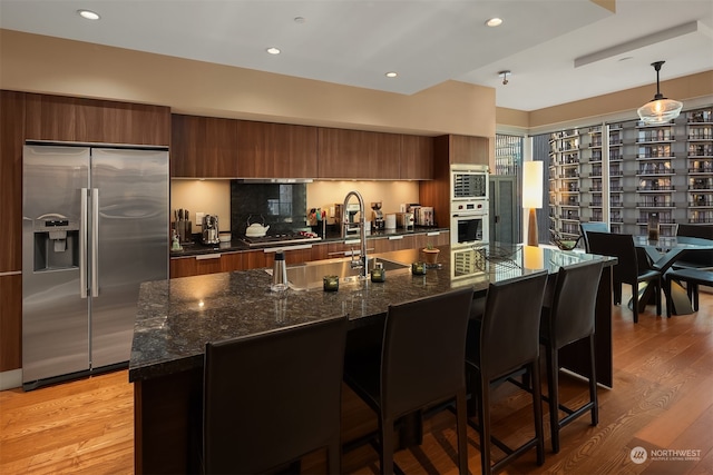 kitchen featuring appliances with stainless steel finishes, light wood-type flooring, a breakfast bar, a center island with sink, and hanging light fixtures