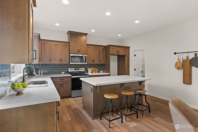 kitchen featuring a kitchen bar, stainless steel appliances, sink, light hardwood / wood-style floors, and a kitchen island