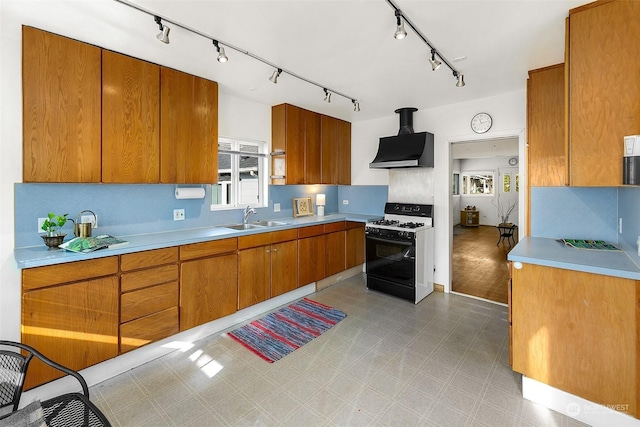 kitchen with range with gas cooktop, light countertops, a sink, and wall chimney exhaust hood