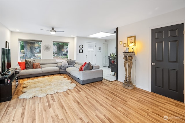 living room featuring light wood-type flooring, a skylight, and ceiling fan