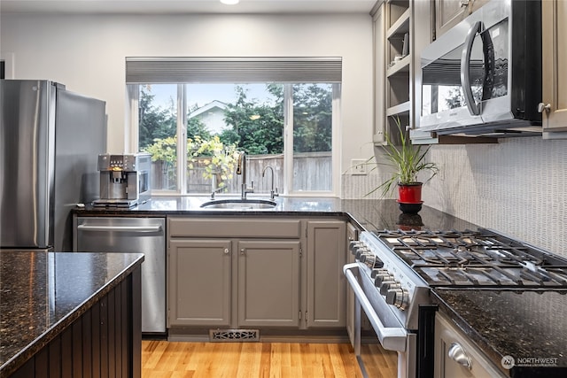 kitchen featuring appliances with stainless steel finishes, sink, light hardwood / wood-style flooring, and dark stone countertops