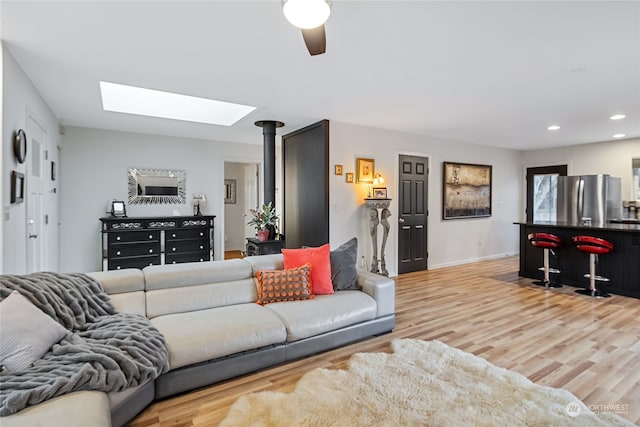 living room featuring a skylight, ceiling fan, and light hardwood / wood-style flooring