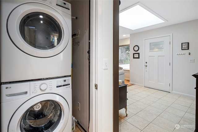 clothes washing area featuring a skylight, stacked washer and dryer, and light tile patterned floors