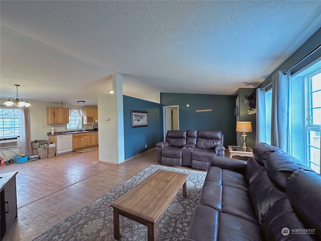 living room with a textured ceiling, vaulted ceiling, sink, a notable chandelier, and light hardwood / wood-style floors