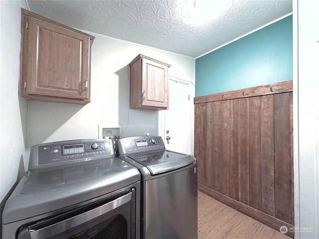 laundry area featuring cabinets, a textured ceiling, washing machine and dryer, and light hardwood / wood-style flooring