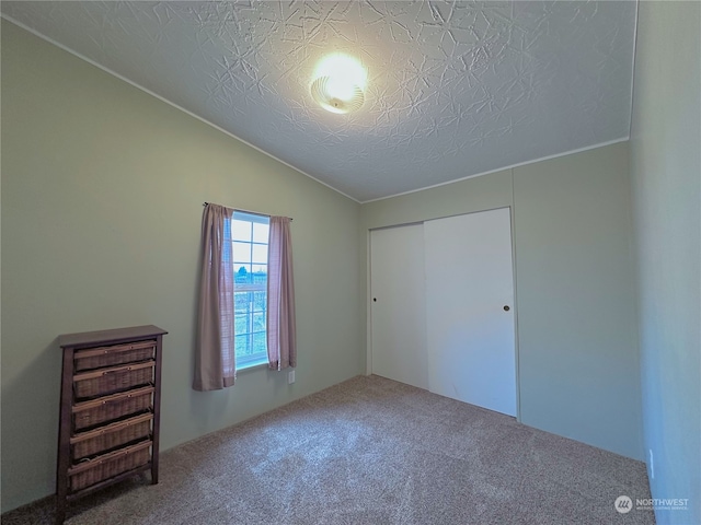 unfurnished bedroom with a textured ceiling, carpet floors, a closet, and lofted ceiling