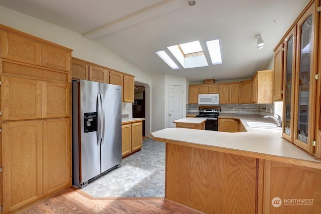 kitchen featuring kitchen peninsula, appliances with stainless steel finishes, lofted ceiling with skylight, sink, and light hardwood / wood-style flooring