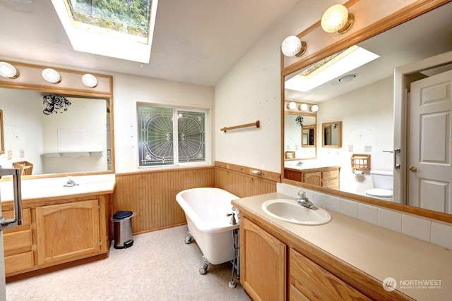 bathroom with vanity, a bathtub, wooden walls, and vaulted ceiling with skylight