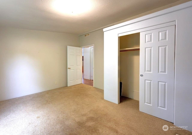 unfurnished bedroom with a textured ceiling, light carpet, and a closet