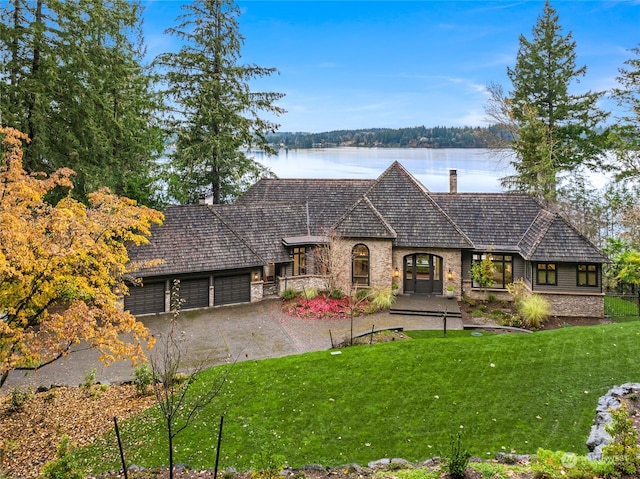 french country home with a garage, a front lawn, and a water view