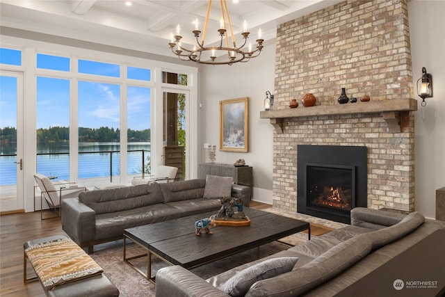 living room with an inviting chandelier, a water view, wood-type flooring, a brick fireplace, and beamed ceiling