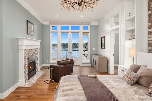 living room featuring a fireplace, ornamental molding, a water view, light wood-type flooring, and french doors