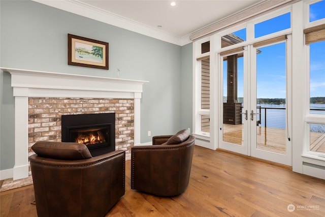 living room with a brick fireplace, crown molding, light hardwood / wood-style flooring, and a water view