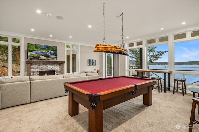 recreation room featuring crown molding, plenty of natural light, a water view, a brick fireplace, and light colored carpet