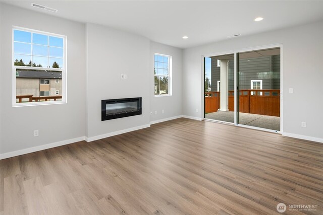 unfurnished living room featuring visible vents, wood finished floors, baseboards, and a glass covered fireplace