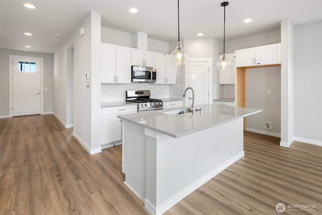 kitchen featuring a sink, light wood-style floors, white cabinets, stainless steel appliances, and a kitchen island with sink