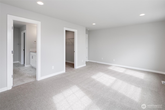 unfurnished bedroom featuring recessed lighting, a walk in closet, baseboards, and light colored carpet