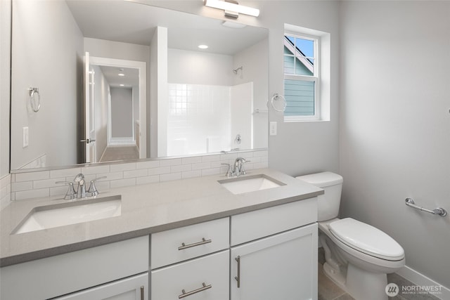 full bath with decorative backsplash, double vanity, toilet, and a sink